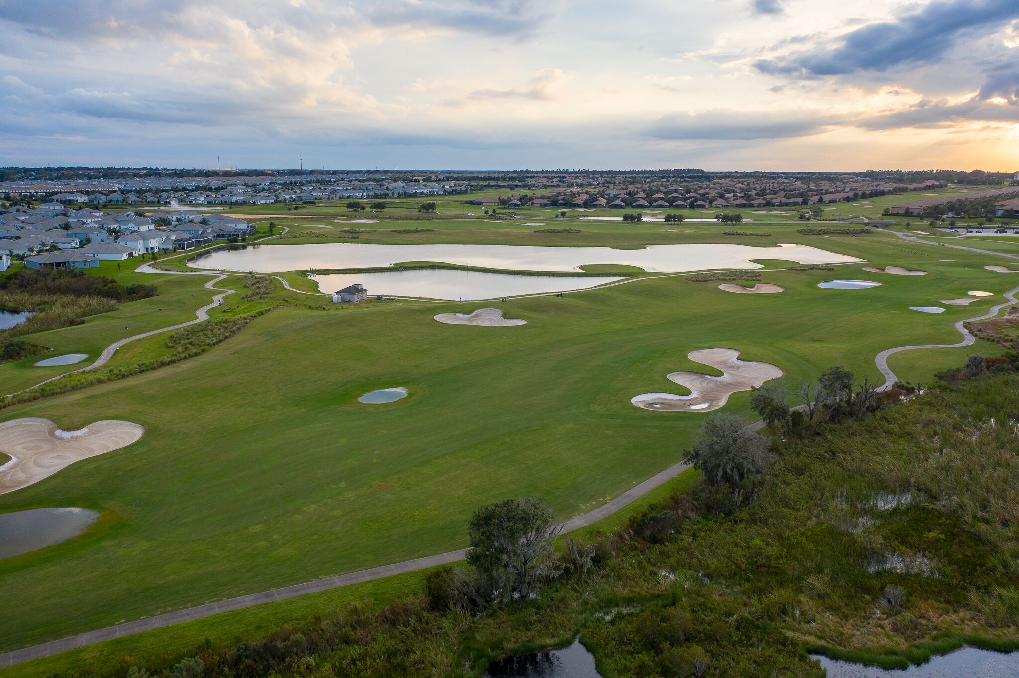 Um campo de golfe com vários bunkers, obstáculos de água e um green bem cuidado.