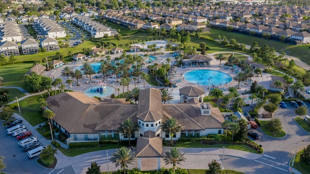 Vista aérea de un conjunto residencial con varias casas, una piscina central y un edificio grande con un techo distintivo.