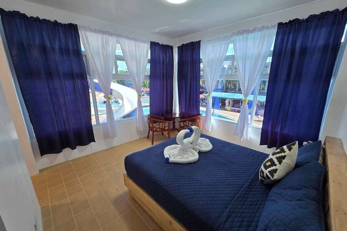 A hotel room with a bed, a chair, and a view of an outdoor swimming pool.