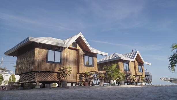 Ein Holzstrandhaus mit geneigtem Dach, großen Fenstern und Sitzgelegenheiten im Freien.