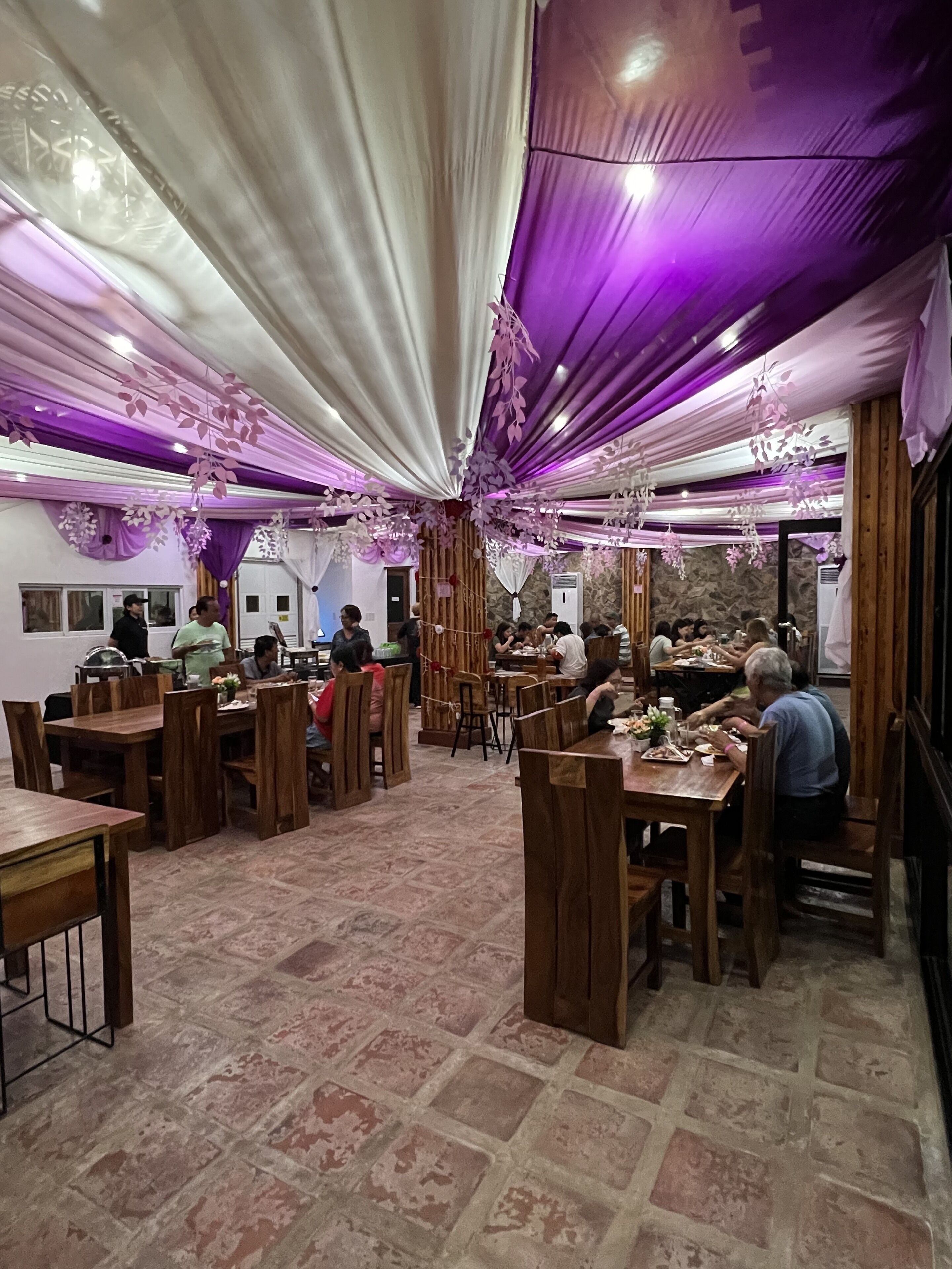 A restaurant with wooden tables and chairs, purple drapes, and hanging decorations.