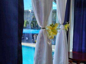 Habitación con vista a una piscina, cortinas recogidas y una pequeña mesa.
