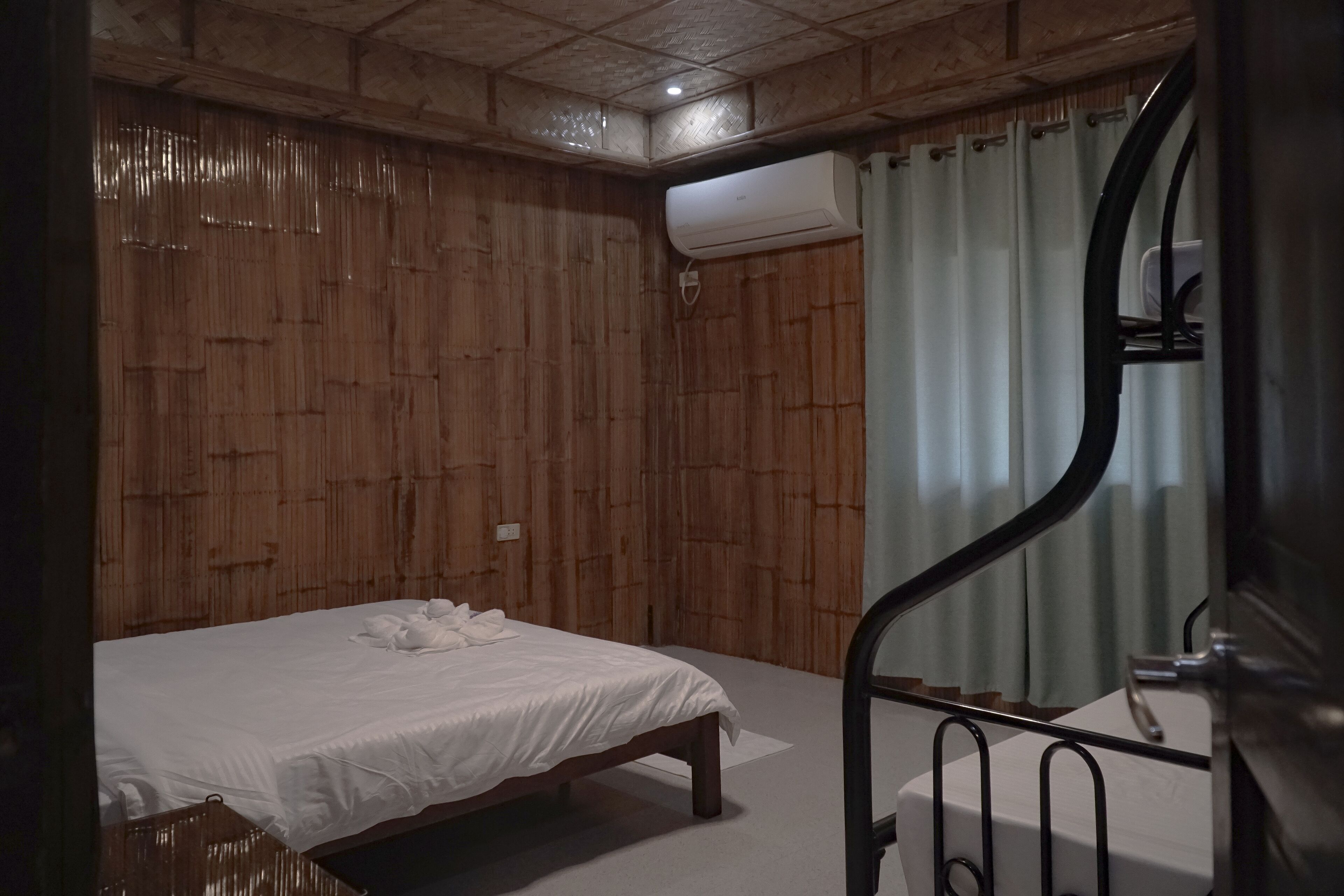 A bedroom with a wooden wall, a bed with white bedding, a metal staircase, and an air conditioning unit.