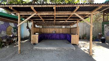 Un espacio de estar al aire libre cubierto, con suelo de concreto y estructura de madera.