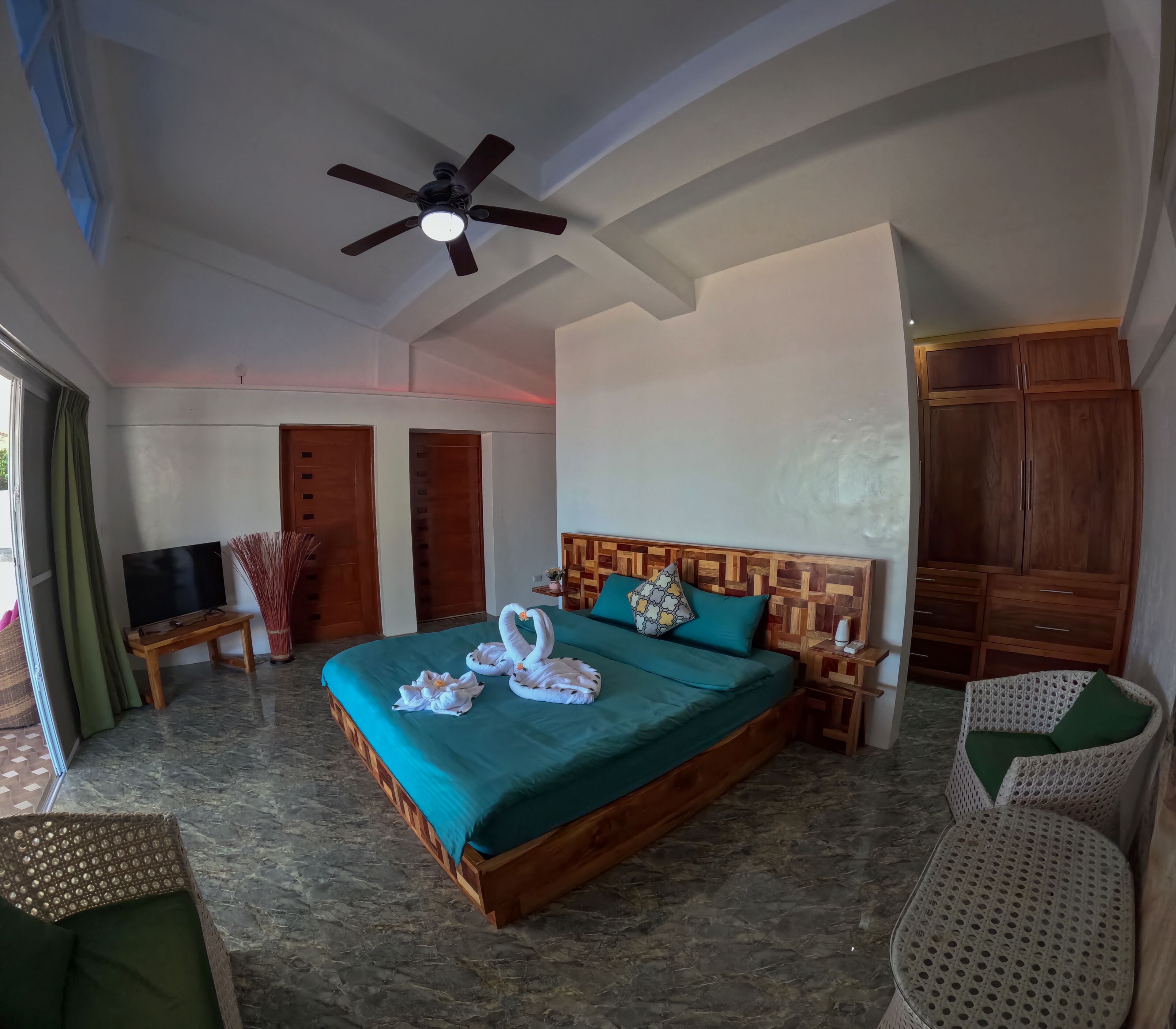 A spacious bedroom with a large bed, wooden headboard, a ceiling fan, and a wardrobe.
