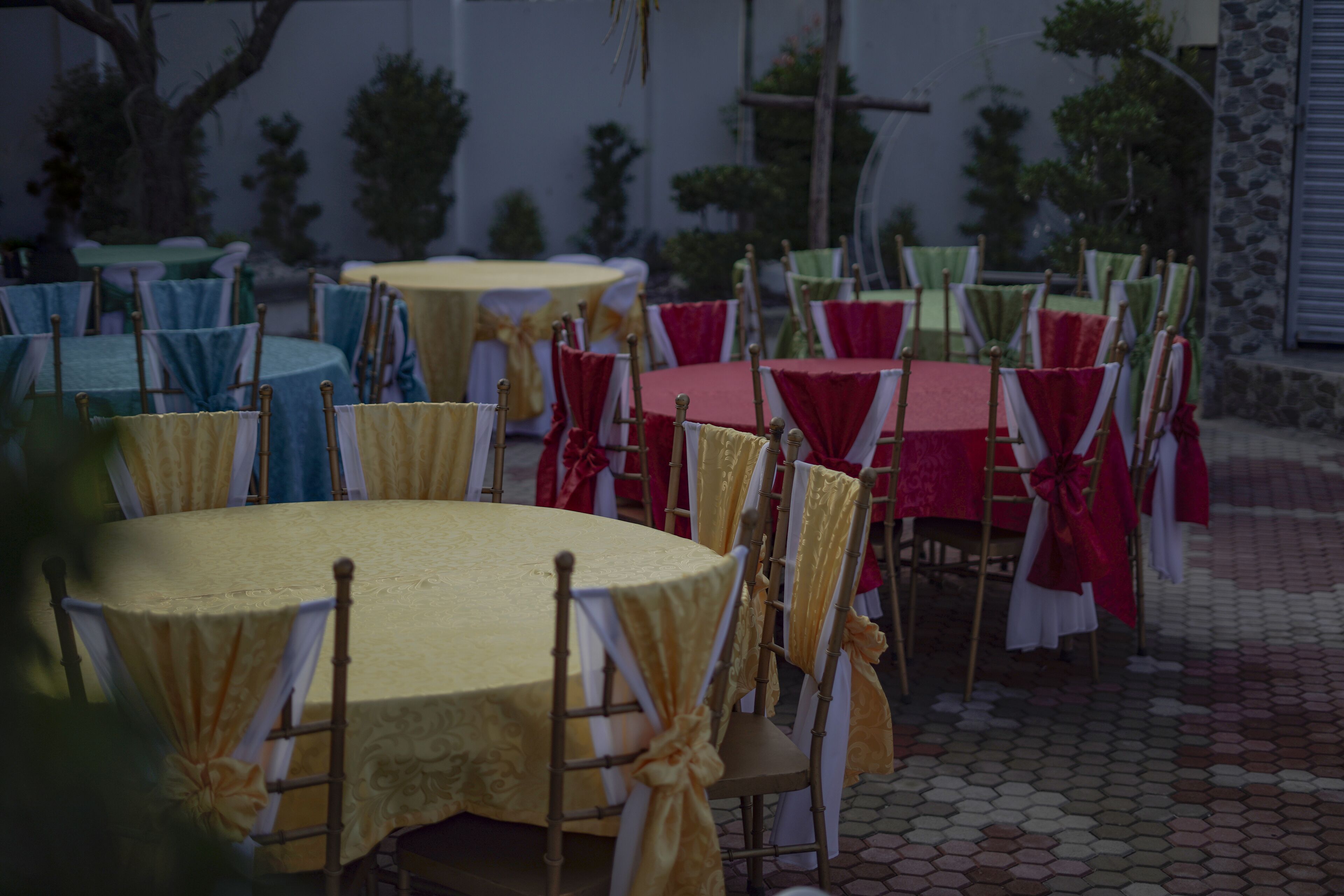 A series of round tables with chairs, each table covered with a different colored tablecloth and chairs draped with white and gold sashes.