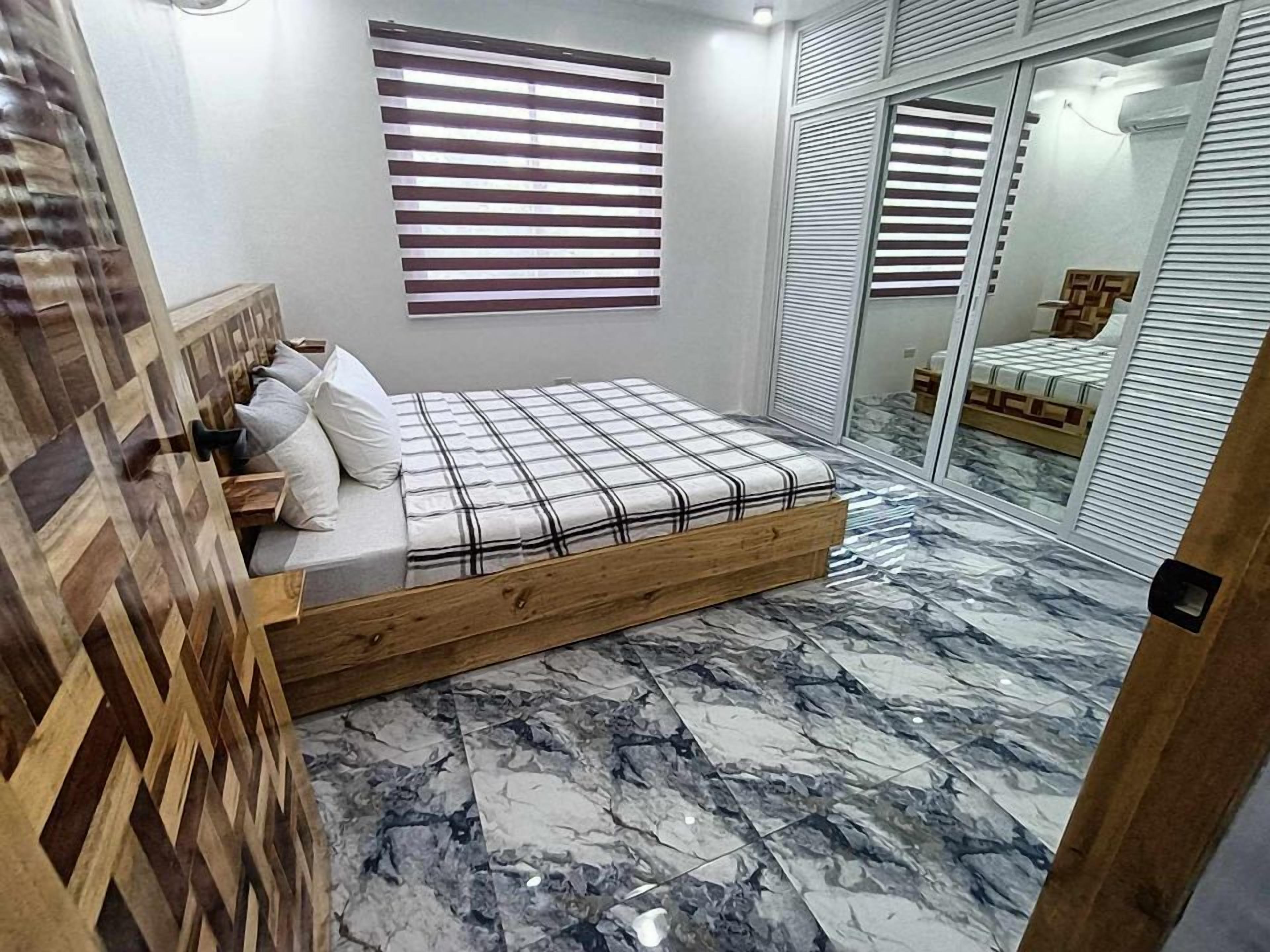 A bedroom with a wooden bed, a marble floor, and a sliding glass door leading to a bathroom.