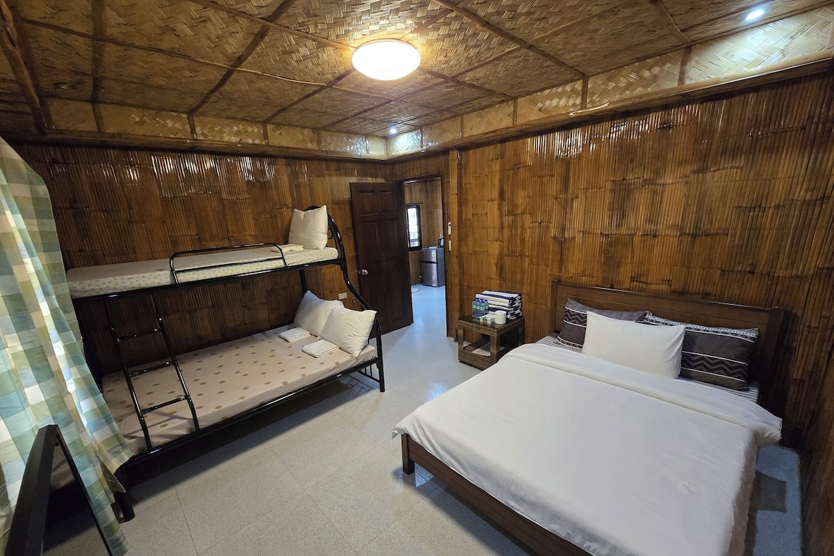 A room with bunk beds, a single bed, a small table with items, and a wooden ceiling.