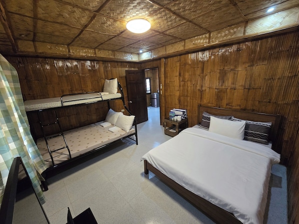 Ein Zimmer mit Etagenbetten, einem Einzelbett, einem kleinen Tisch mit Gegenständen und einer Holzbalkendecke.
