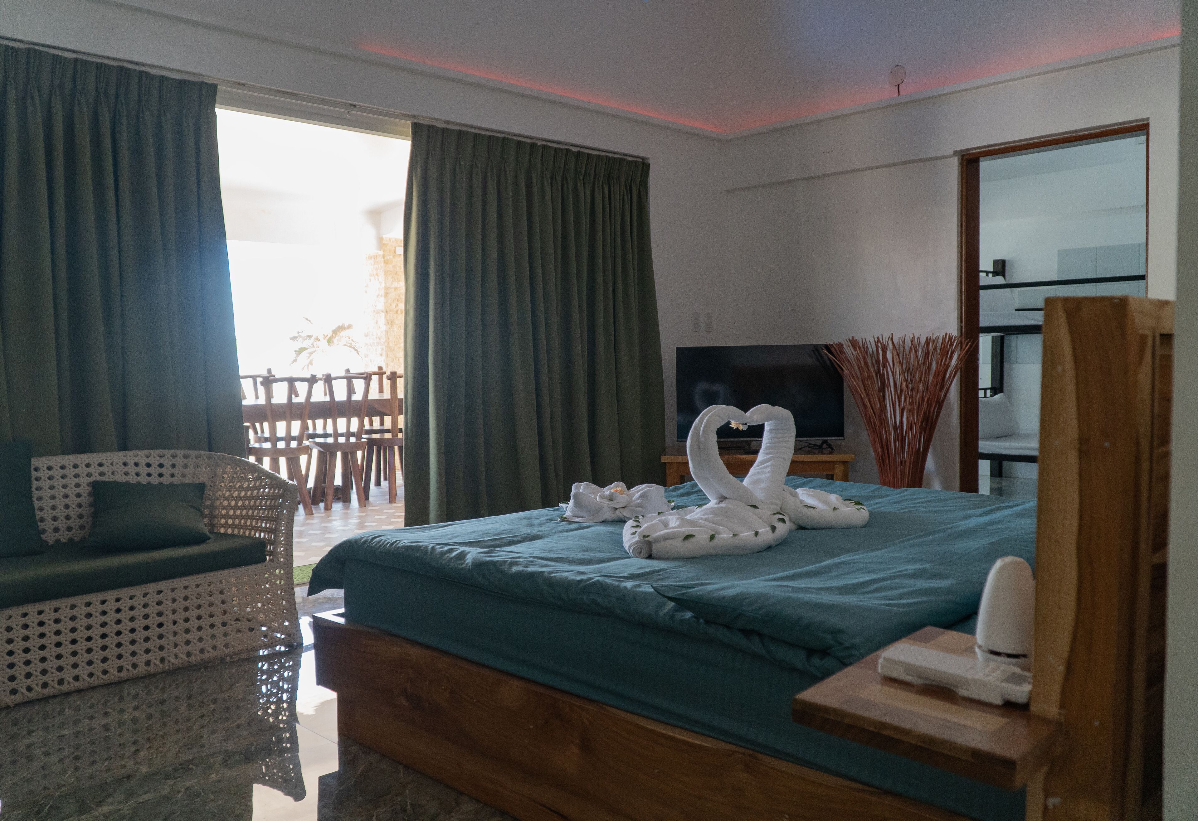 A hotel room with a bed, a TV, a wooden side table, and a seating area with a sofa and chairs.