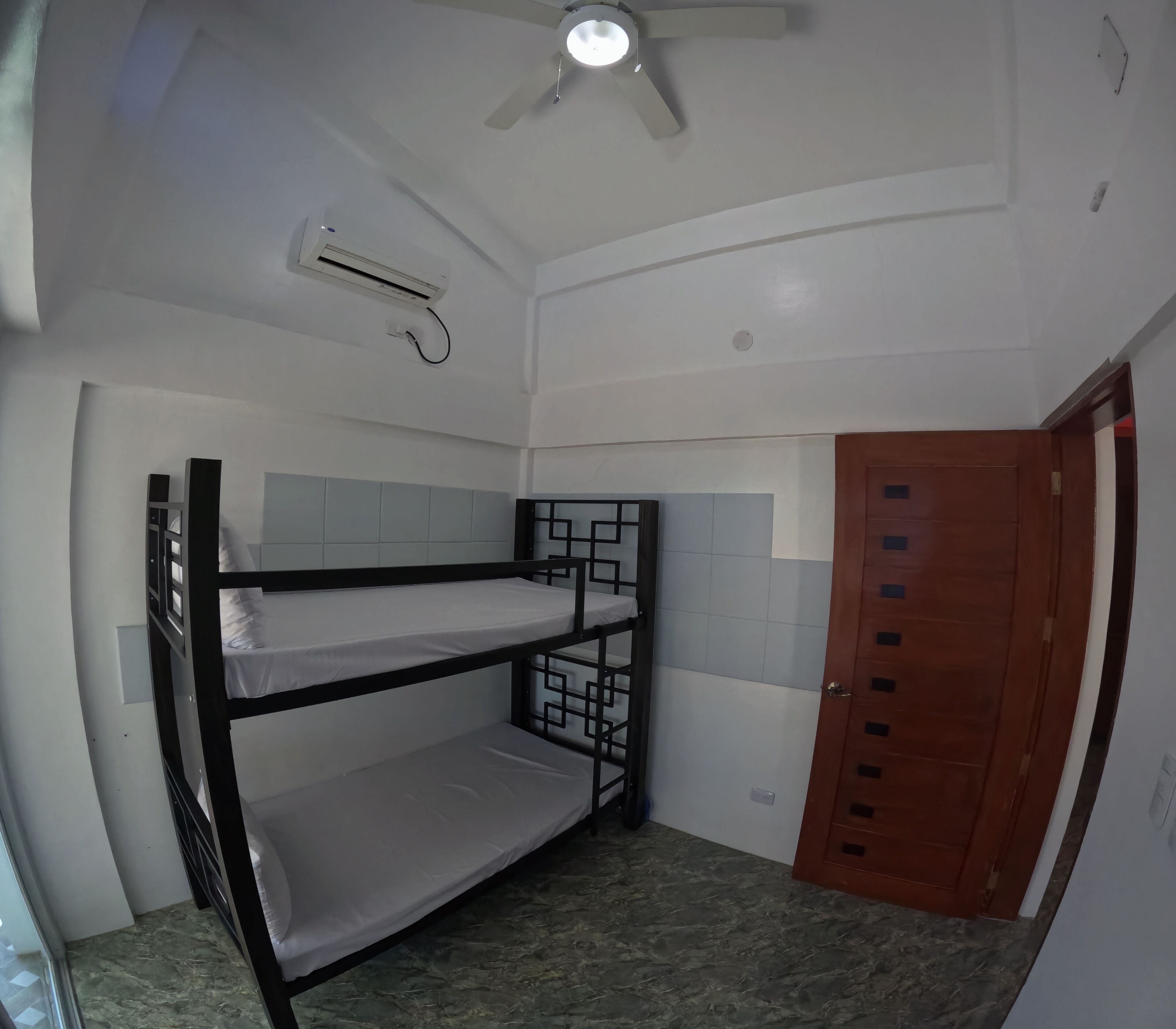 Habitación con literas, ventilador de techo, aire acondicionado y puerta de madera.