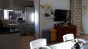 Une cuisine compacte dotée d’appareils électroménagers modernes, un coin repas avec une table et des chaises, et un espace de vie agrémenté d’un téléviseur et d’objets décoratifs.