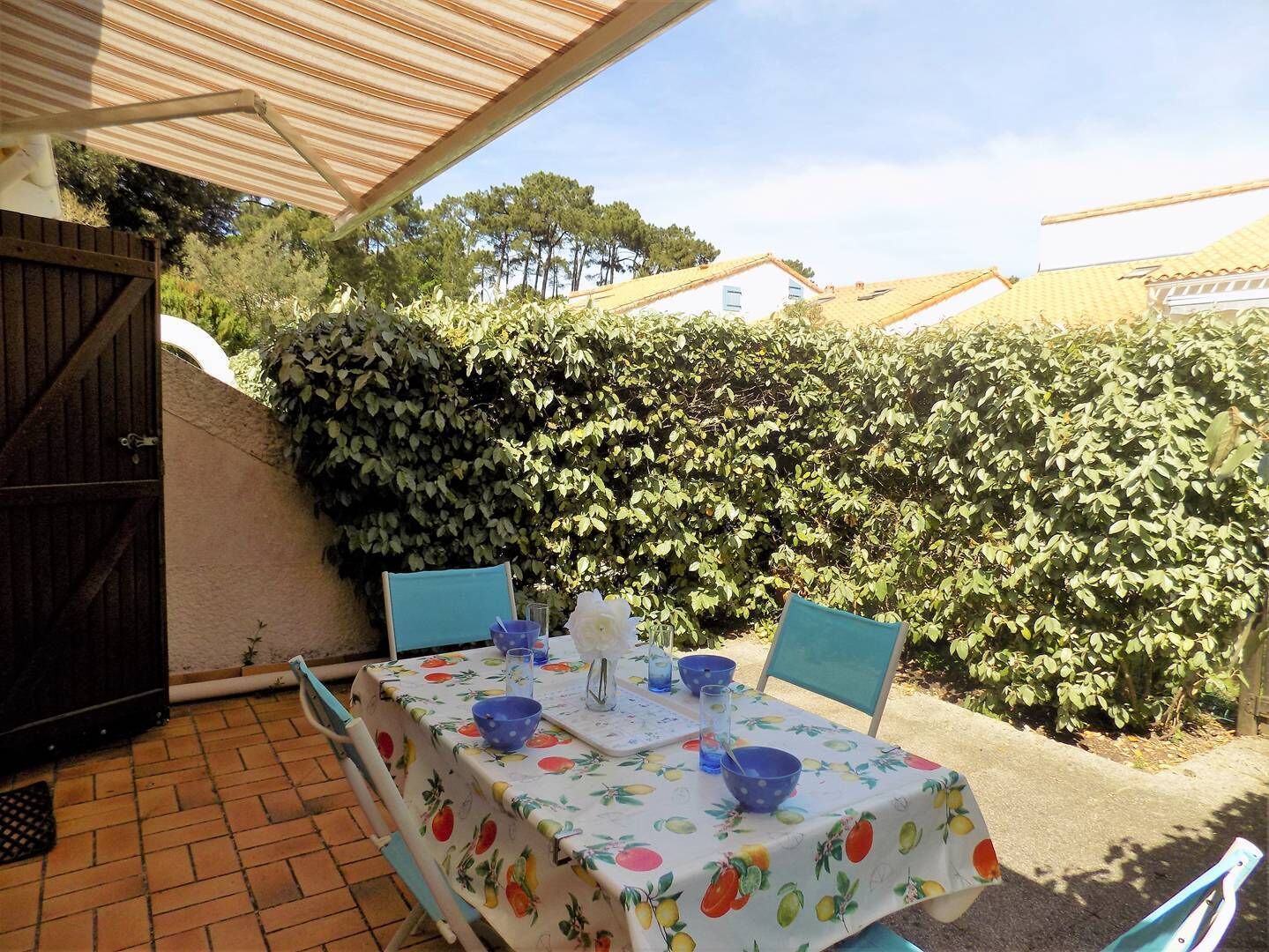 Eine Terrasse im Freien mit Tisch für zwei Personen, umgeben von einem Hecken und einem Holzzaun.