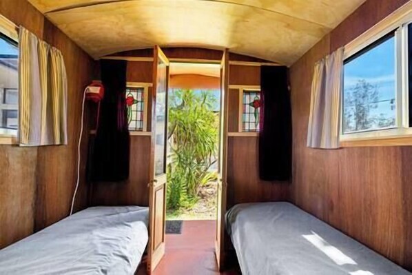 A cabin with two beds, wooden walls, and windows with curtains.