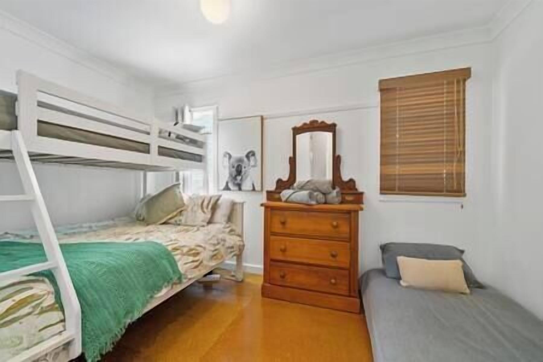 Een kleine slaapkamer met stapelbedden, een dressoir en een eenpersoonsbed.