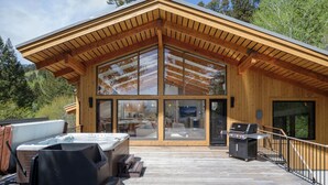 En stuga byggd av trä med ett stort glasfönster, en bubbelpool och en grillplats.