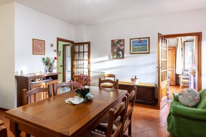 A dining area with a wooden table and chairs, a green armchair, and a view of the kitchen through an open door.