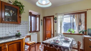 Un coin repas avec une table dressée pour quatre personnes, une cuisine avec des meubles en bois et une vue sur l’extérieur par une fenêtre.