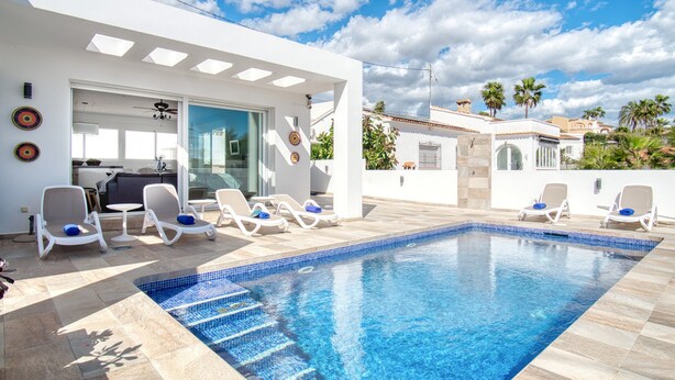 Una piscina moderna all'aperto con lettini, un ingresso con porta in vetro e un cielo azzurro.