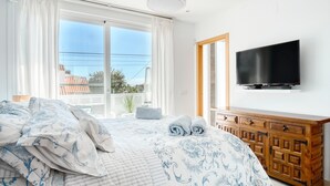 Una camera da letto con un letto grande, una cassettiera in legno, una TV a schermo piatto e una finestra vista edifici.