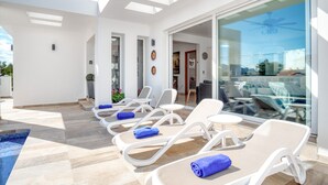 Un'area lounge esterna moderna con lettini e una porta vetrata che dà su una piscina.