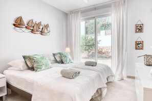 A bedroom with two beds, a window with curtains, a wall-mounted artwork of sailboats, and a small bedside table.