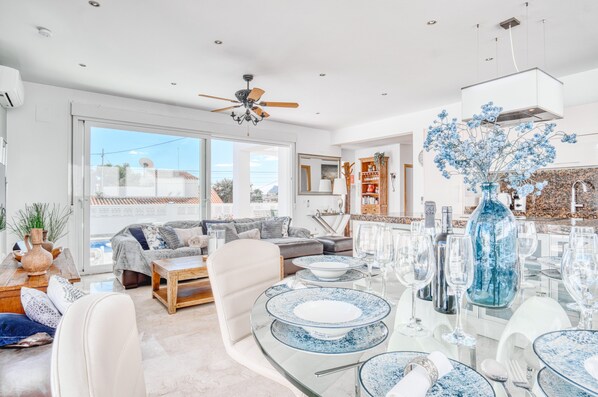 A modern living room with a dining area, large windows, and a ceiling fan.