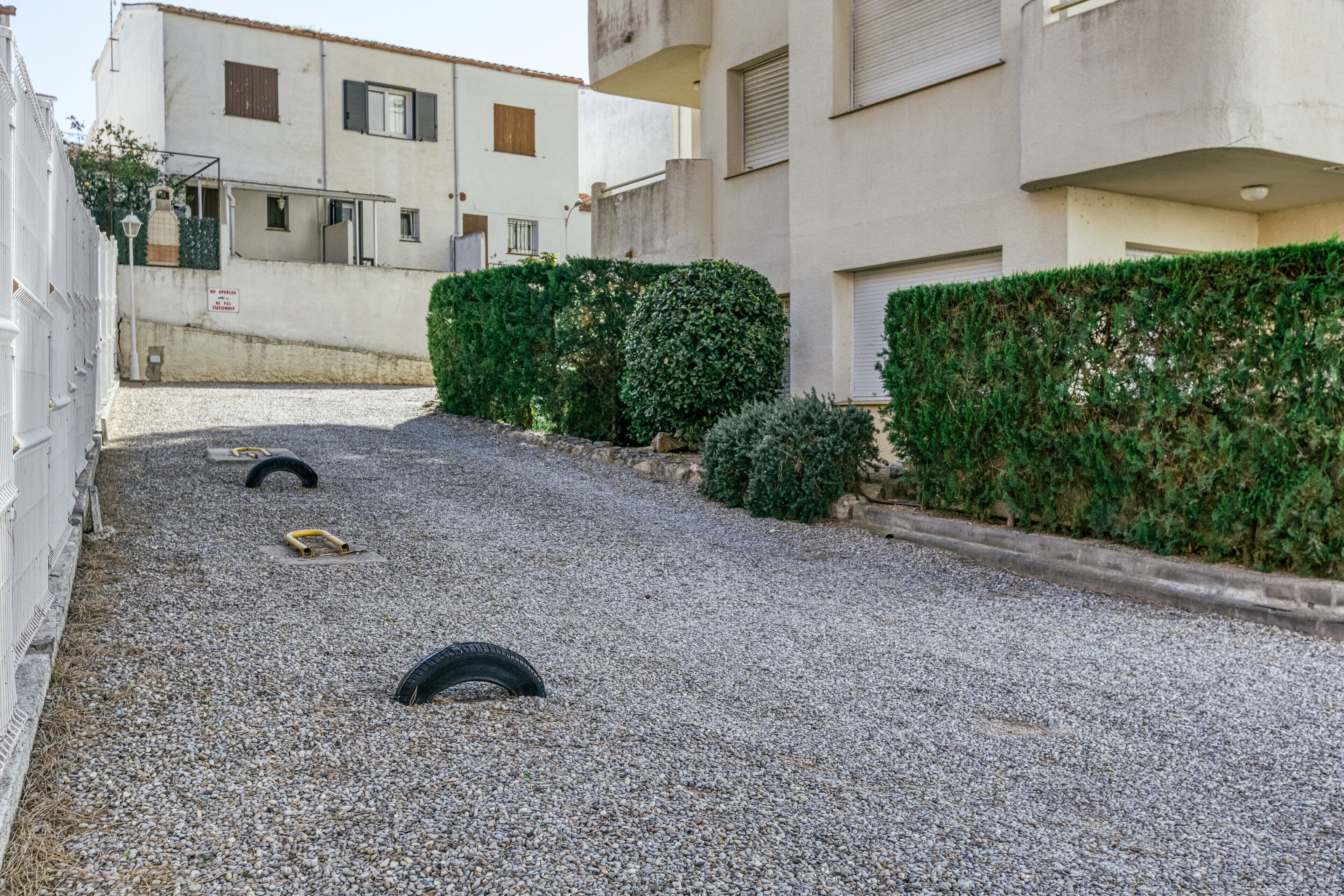Un patio con piso de grava, un seto y un edificio con varias ventanas y balcones.