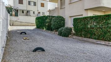 Un patio con piso de grava, un seto y un edificio con varias ventanas y balcones.
