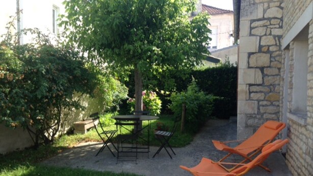 Een terras met een tafel, stoelen, een boom en een stenen muur.