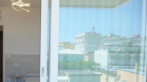 A bedroom with a bed, bedside table, and a view of buildings through a glass door. - Apartment 'Residence Bafjle 42' with Shared Pool, Private Terrace and Air Conditioning (Jesolo)