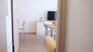 A hallway leading to a dining area with a TV, chairs, and a potted plant.