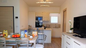 A compact kitchen with a microwave, oven, and sink, a dining area with chairs and a table, and a TV on the right.