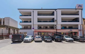 A multi-story building with a 'dm' sign, a parking lot with several cars, and a no parking sign.
