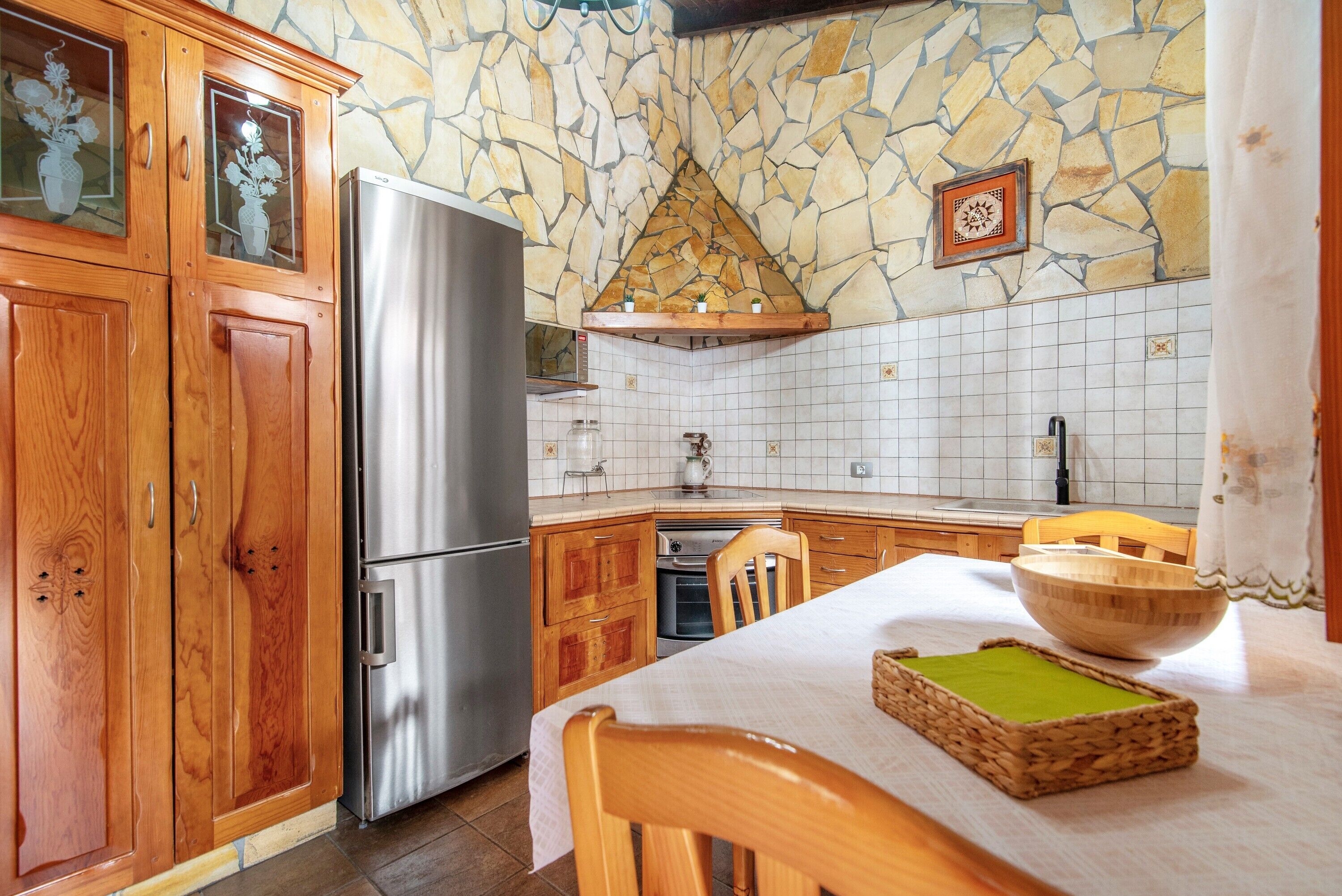 A kitchen with wooden cabinets, a stainless steel refrigerator, a stone backsplash, and a tiled backsplash.