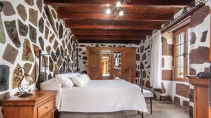 Ein Schlafzimmer mit Steinwand, Holzboden, einem Bett mit weißer Bettwäsche, einem Nachttisch und einem Fenster mit Vorhängen.