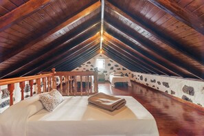 Une chambre aménagée dans les combles, avec un plafond en bois, un lit avec un oreiller, une rambarde en bois et un mur en pierre.