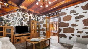 Ein rustikales Interieur mit Steinwänden, Holzmöbeln, einem Flachbildfernseher und einem Essbereich.