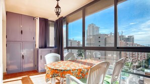 A balcony with a table and chairs, a window with a city view, and a purple cabinet.
