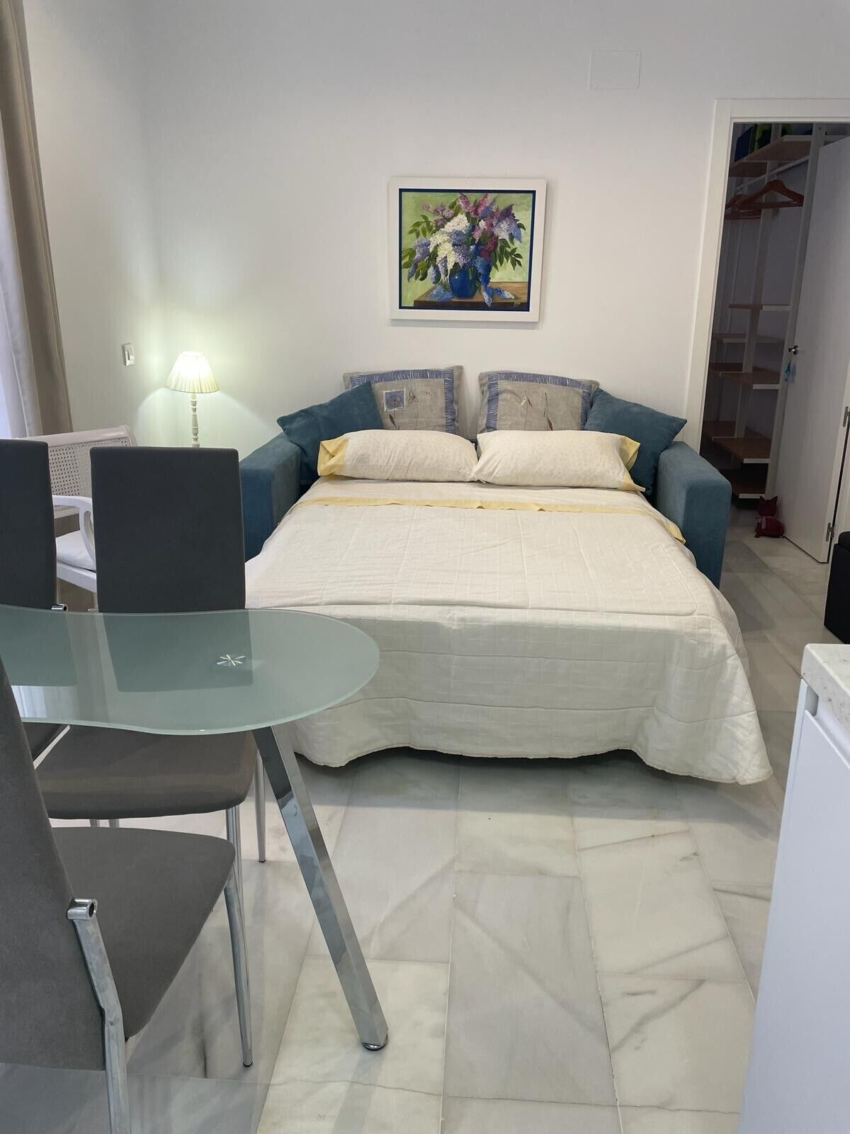 Ein Schlafzimmer mit Bett, Tisch, Stühlen, Lampe und einem Gemälde an der Wand.