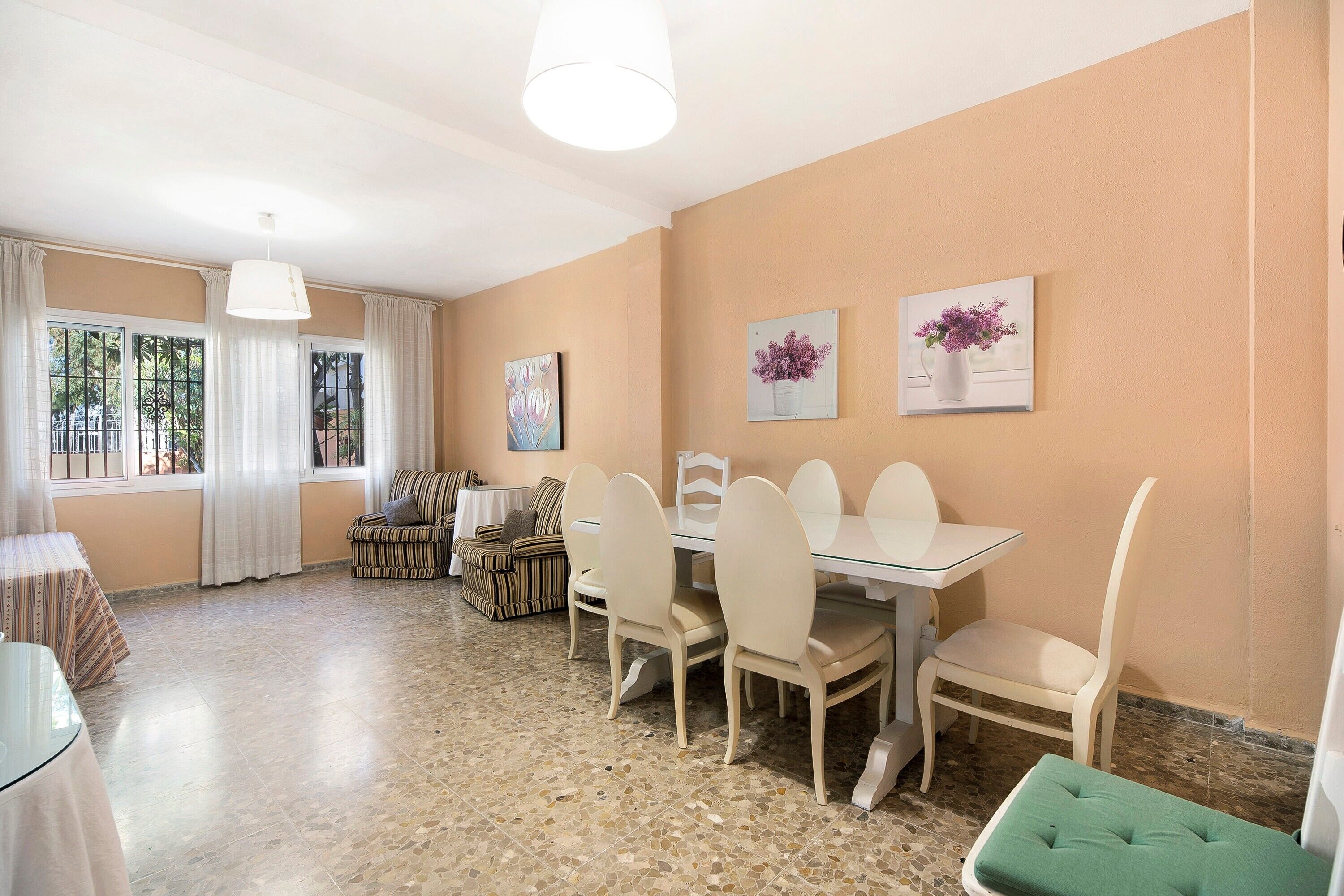 A dining area with a table and chairs, a sofa, and a green ottoman.