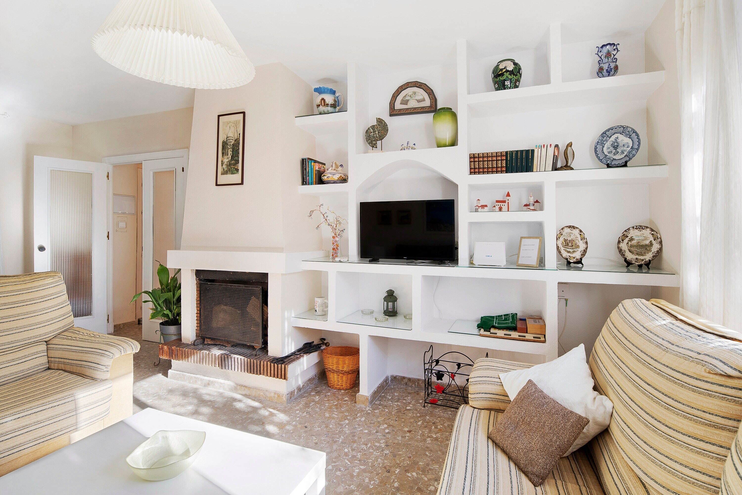 A living room with striped sofas, a flat-screen TV, a fireplace, and a white shelving unit with decorative items.