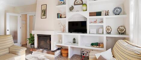 A living room with striped sofas, a flat-screen TV, a fireplace, and a white shelving unit with decorative items.