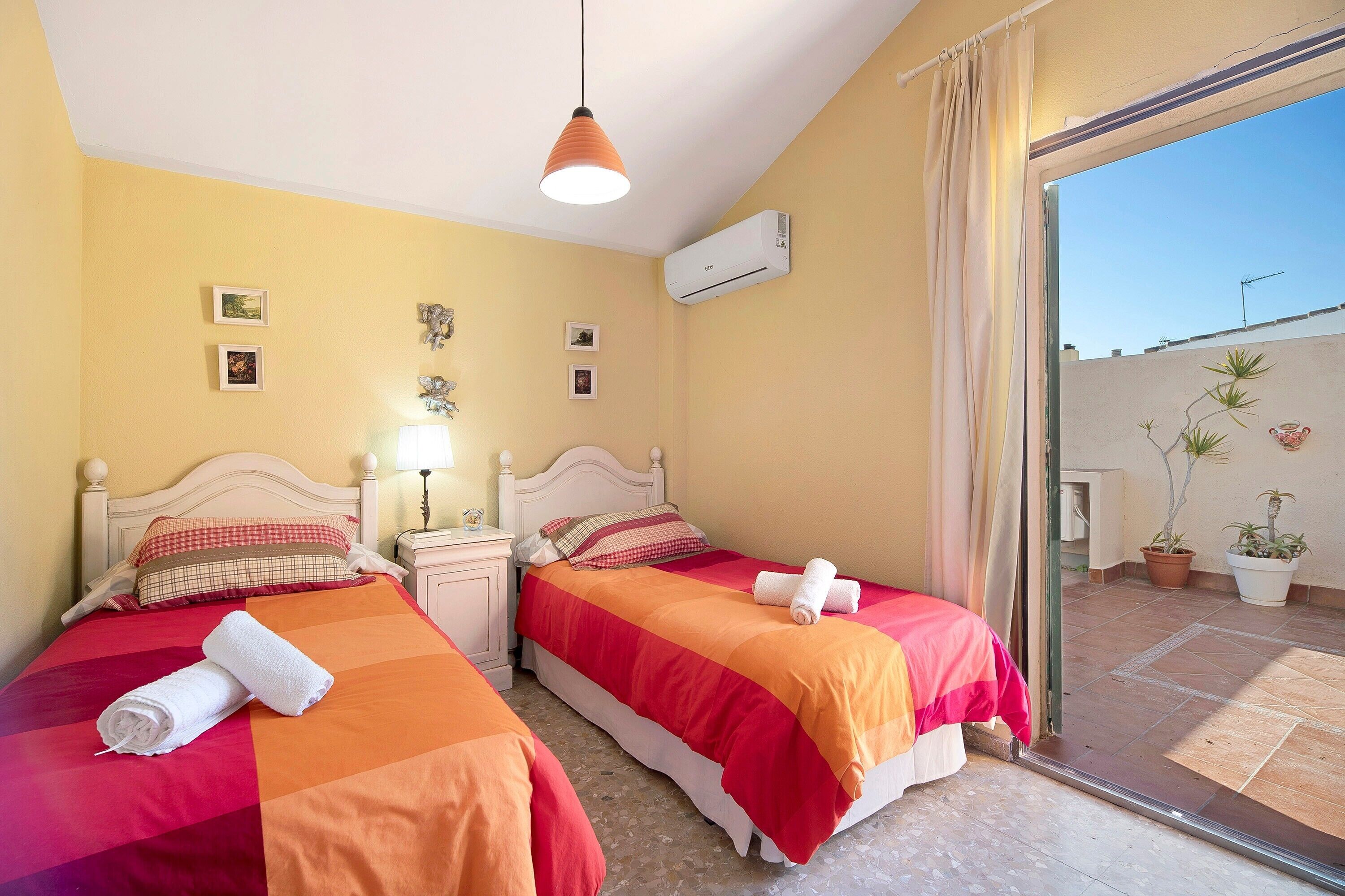 Habitación de hotel con dos camas, un balcón con plantas en macetas y un equipo de aire acondicionado.