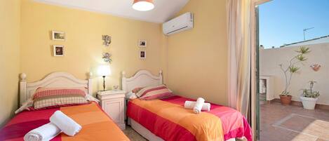 Habitación de hotel con dos camas, un balcón con plantas en macetas y un equipo de aire acondicionado.