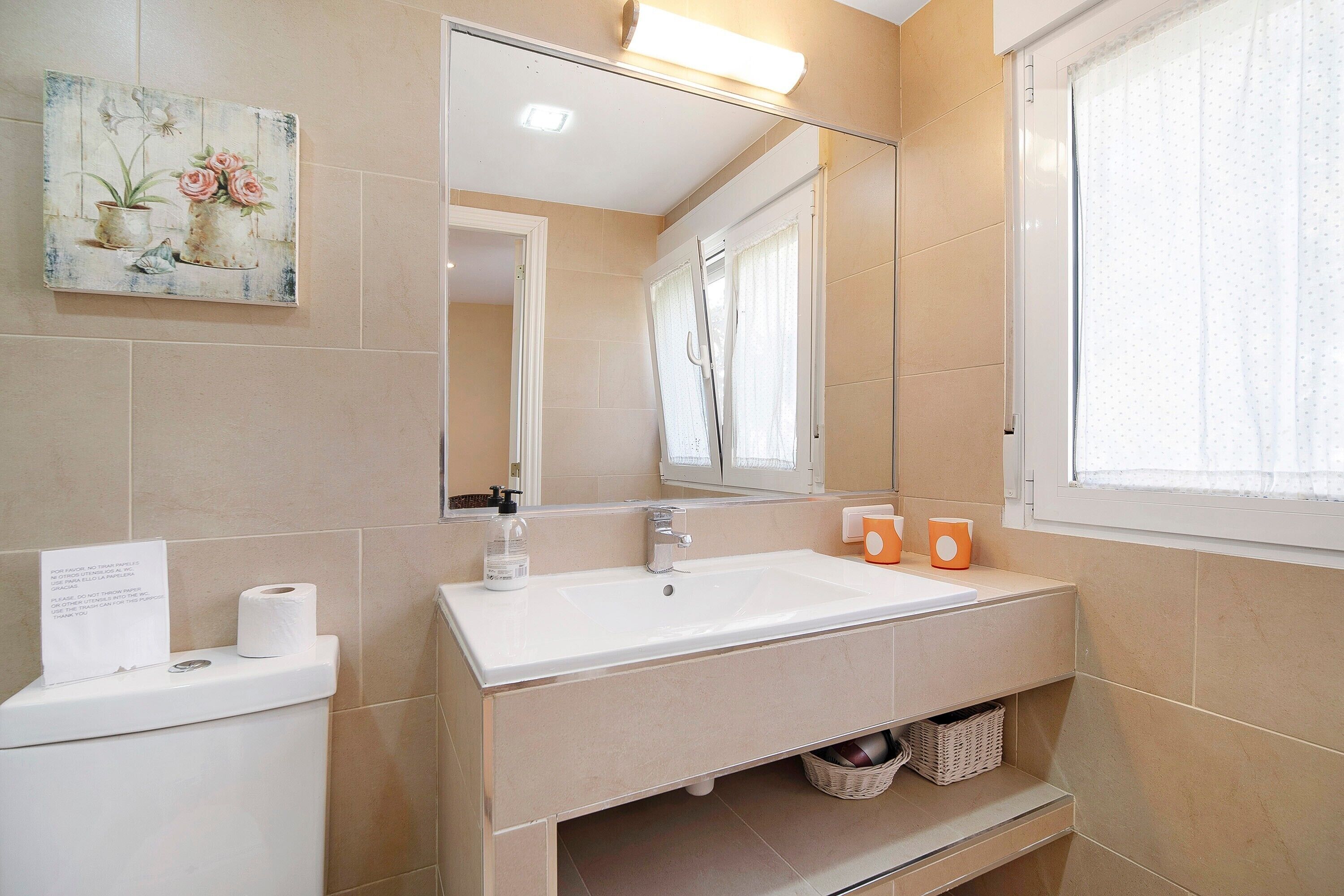Un baño con lavamanos, espejo, papel higiénico y un letrero.