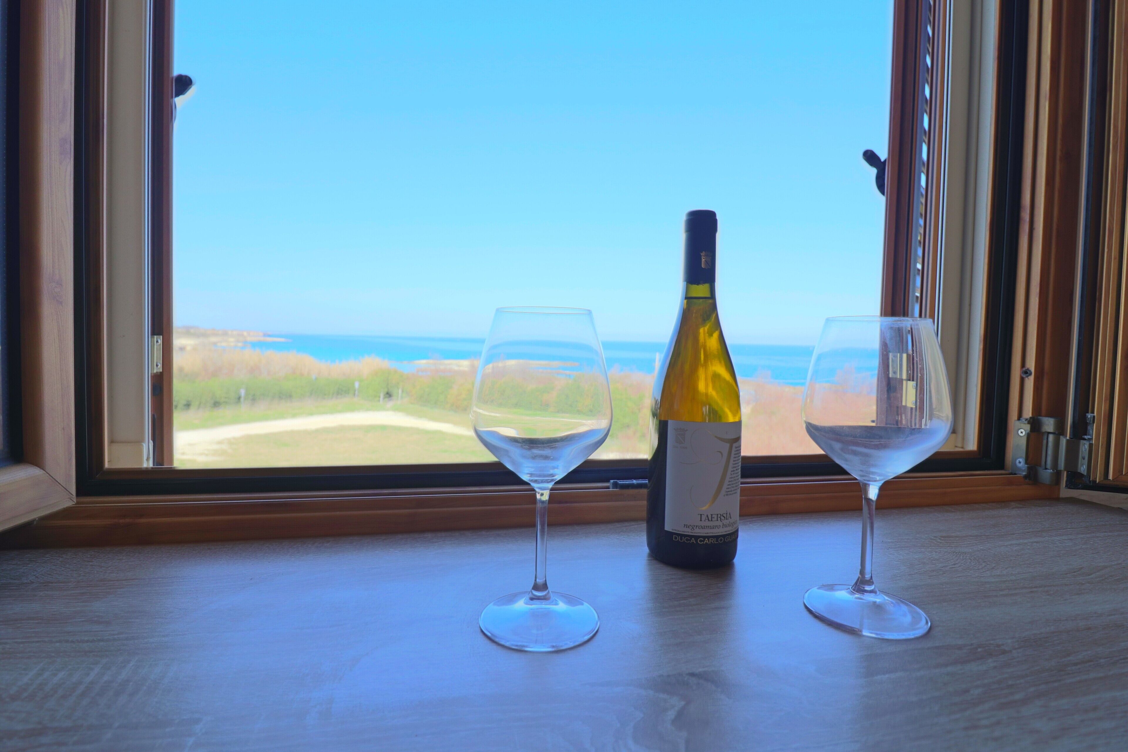 Eine Weinflasche und zwei Gläser auf einem Fensterbrett mit Blick auf das Meer.