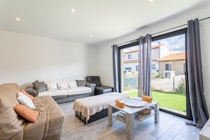A modern living room with a sofa, a bed, a small table, and a large sliding glass door leading to a garden. - Villa Rascola Piscine 4 Stars with private pool, Wi-Fi and air conditioning (Le Boulou)