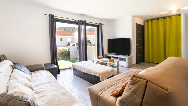 A modern living room with a sofa, a small table, a TV, and a view of the outside. - Villa Rascola Piscine 4 Stars with private pool, Wi-Fi and air conditioning (Le Boulou)