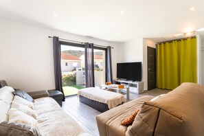 A modern living room with a sofa, a small table, a TV, and a view of the outside. - Villa Rascola Piscine 4 Stars with private pool, Wi-Fi and air conditioning (Le Boulou)